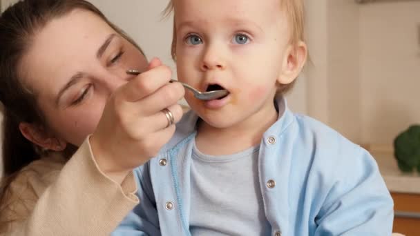 Portret van een kleine jongen die zijn mond opent terwijl hij pap eet met een lepel. Concept van kleine chef-kok, kinderen koken voedsel, gezonde voeding — Stockvideo