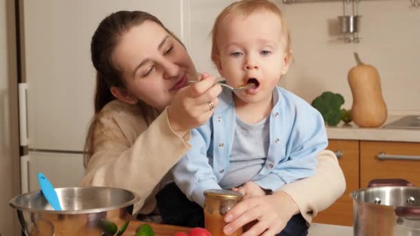 Ibu yang penuh kasih memberi makan bayi laki-lakinya bermain dengan peralatan masak di dapur. Konsep koki kecil, anak-anak memasak makanan, nutrisi yang sehat — Stok Video