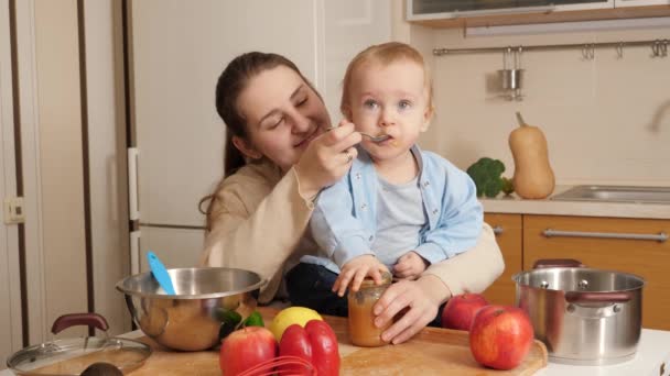 Kleine baby jongen zittend op keukentafel en spelen met keukengerei en kookgerei tijdens het eten van lepel. Concept van kleine chef-kok, kinderen koken voedsel, gezonde voeding — Stockvideo