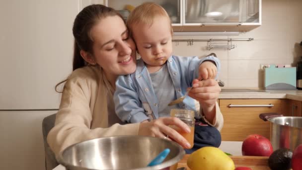 Little baby boy taking spoon while mother is trying to feed him on kitchen. Concept of healthy nutrition,diet and children food — Stock Video