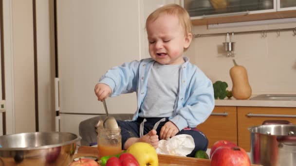 Mały płaczący chłopczyk próbujący zjeść owsiankę łyżką w kuchni. Pojęcie zdrowego odżywiania, diety i żywności dla dzieci — Wideo stockowe