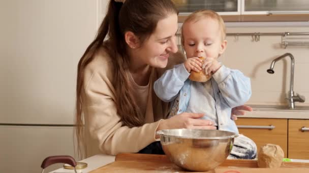 Bonito menino sorridente com a mãe comendo pão fresco e brincando com farinha. Conceito de pequeno chef, crianças cozinhar alimentos, nutrição saudável. — Vídeo de Stock