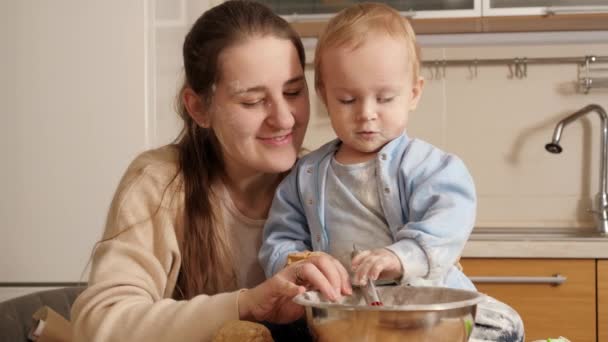 小さな赤ちゃんの男の子は、母親が生地を作り、キッチンでパンを焼くのを手伝っています。小さなシェフ、子供たち料理、健康的な栄養の概念. — ストック動画