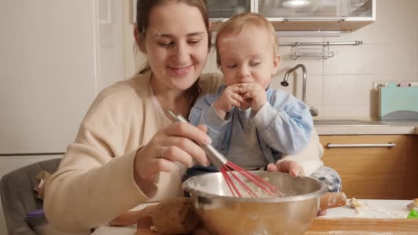 Mały chłopczyk, wyglądający jak uśmiechnięta matka, ugniatający ciasto w misce w kuchni. Pojęcie małego kucharza, dzieci gotujące jedzenie, zdrowe odżywianie. — Wideo stockowe