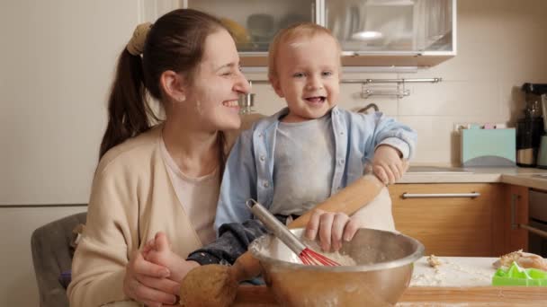 Gelukkige lachende baby jongen met moeder kneden deeg voor het bakken van brood in de keuken. Concept van kleine chef-kok, kinderen koken voedsel, gezonde voeding — Stockvideo