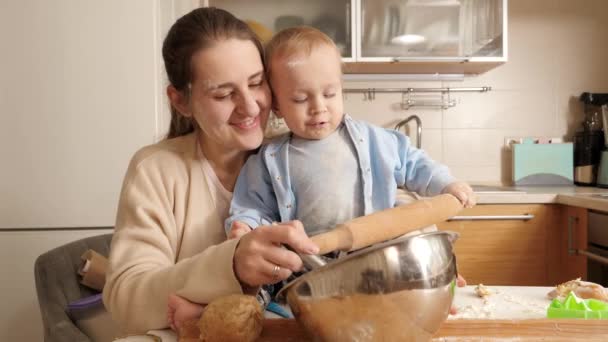 Petit garçon aidant la mère à pétrir la pâte et tenant rouleau à pâtisserie pour la cuisson du pain sur la cuisine. Concept de petit chef, cuisine pour enfants, alimentation saine. — Video