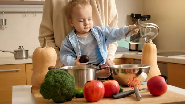 Simpatico bambino sorridente con la madre che gioca con padelle e utensili sul tavolo della cucina. Concetto di piccolo chef, cucina per bambini, buon tempo in famiglia insieme. — Foto Stock