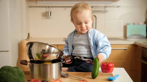 Μικρό αγοράκι 1 έτους που παίζει με λαχανικά στο τραπέζι της κουζίνας — Φωτογραφία Αρχείου