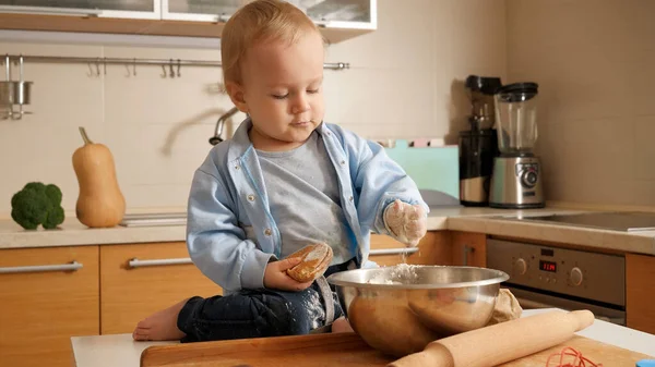 Lustiger kleiner Junge, der mit Mehl in der Schüssel spielt, während er Brot in der Küche kocht. Konzept des kleinen Kochs, der Kinder beim Kochen, der gesunden Ernährung. — Stockfoto