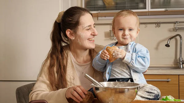 Ritratto di felice madre sorridente con bambino ricoperto di farina e pasta torta di cottura in cucina — Foto Stock