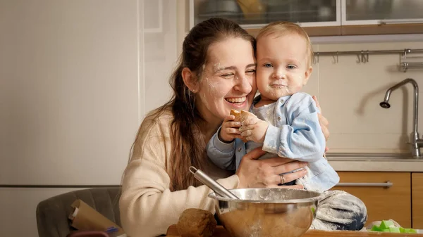 Ritratto di felice madre sorridente che abbraccia il suo bambino ricoperto di pasta e farina mentre cuoce la torta o il pane a casa — Foto Stock