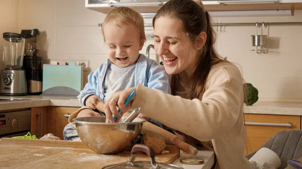 Szczęśliwa uśmiechnięta matka bawiąca się i bawiąca ze swoim małym synkiem podczas robienia ciasta i pieczenia ciasta w kuchni. Pojęcie małego kucharza, dzieci gotujące jedzenie, zdrowe odżywianie. — Zdjęcie stockowe