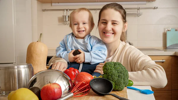 Portrét šťastné usmívající se matky s malým synkem baví v kuchyni při vaření. Koncept malého šéfkuchaře, děti vařící jídlo, dobré společné rodinné chvíle — Stock fotografie
