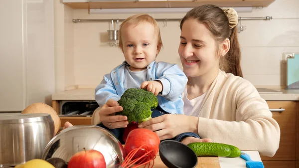 Ritratto di bambino sorridente con giovane madre seduta sul tavolo della cucina e contenente ingredienti per piatti — Foto Stock