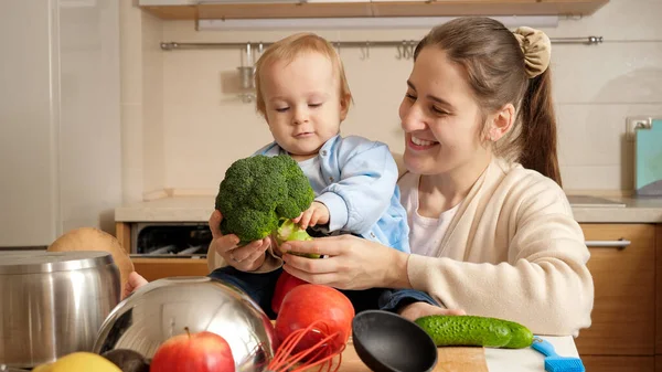 Madre sorridente con bambino che suona e canta canzoni con verdure e frutta in cucina. Concetto di piccolo chef, cucina per bambini, buon tempo in famiglia insieme. — Foto Stock