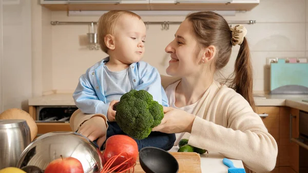 Portrét roztomilého chlapečka usmívajícího se na matku, zatímco ona vaří na kuchyni — Stock fotografie
