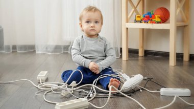 Küçük bebek evde elektrik prizleri ve kablolarla oynuyor..