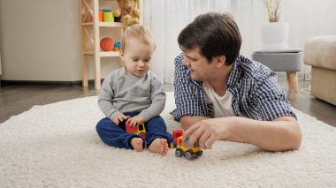 Smiling young man playing with his baby boy with toys at home
