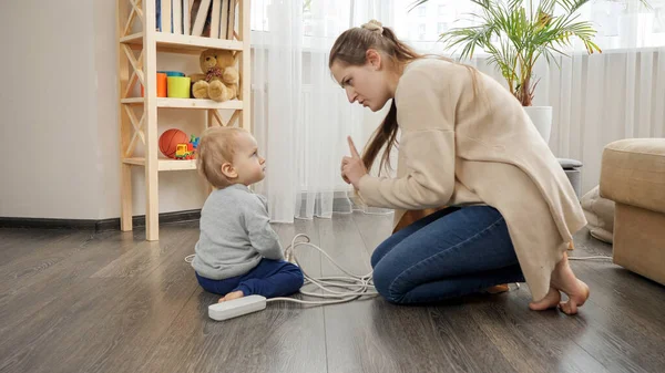 Joven madre cariñosa diciéndole a su hijo bebé que no juegue con electricidad —  Fotos de Stock