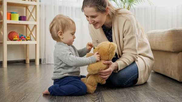 Счастливая улыбающаяся мать учит своего маленького сына и играет с плюшевым мишкой — стоковое фото