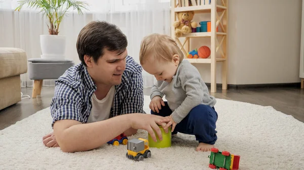 Mały chłopiec daje zabawki ojcu za zabawę na dywanie. — Zdjęcie stockowe