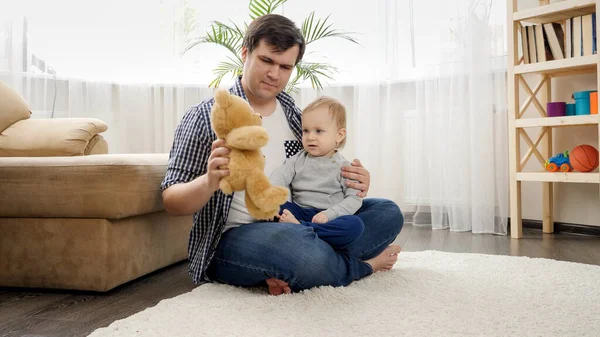 Happy uśmiechnięty chłopiec z ojcem zabawy i zabawy z misia na dywanie w domu. — Zdjęcie stockowe
