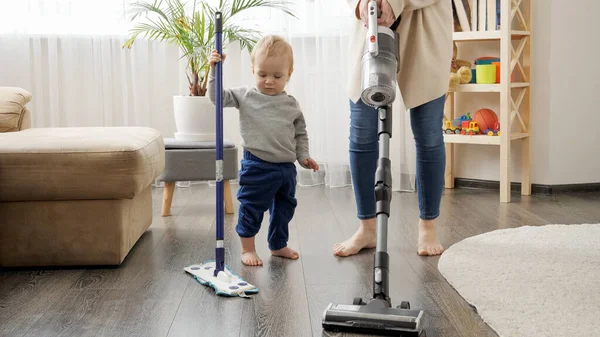 Little baby boy helping his mother doing cleanup at home and vacuming carpet. — Zdjęcie stockowe