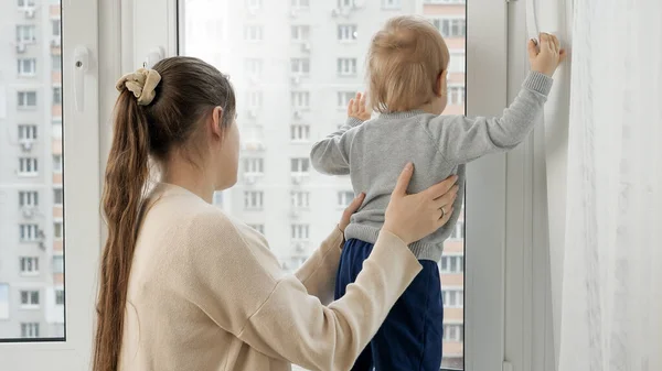 Little baby boy with mother looking out of the window of high store building. — Stok fotoğraf
