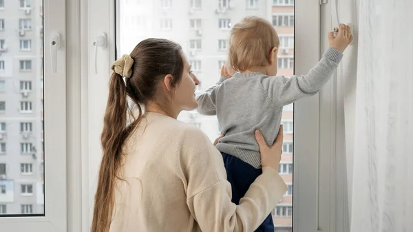Young mother with her baby son walking out of the window at house — Stock Photo, Image