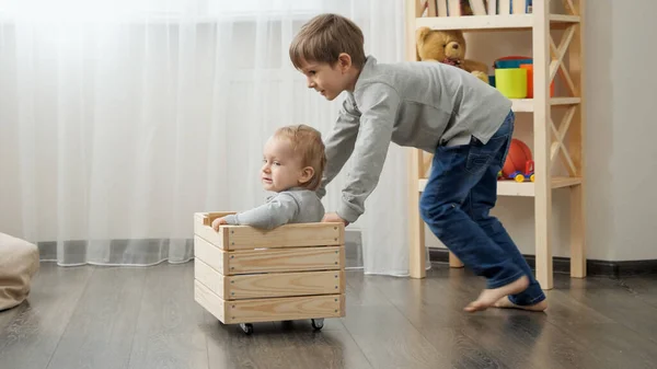 Due fratelli che giocano e cavalcano in scatola di legno. Bambini che giocano e si divertono a casa — Foto Stock