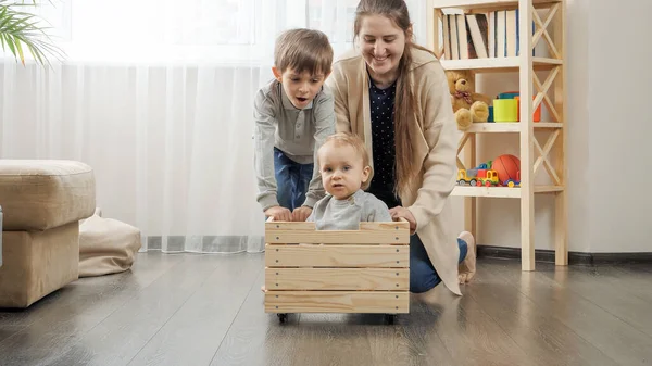 Schattige baby jongen zitten in houten speelgoed doos terwijl zijn familie rijden hem in de woonkamer. — Stockfoto
