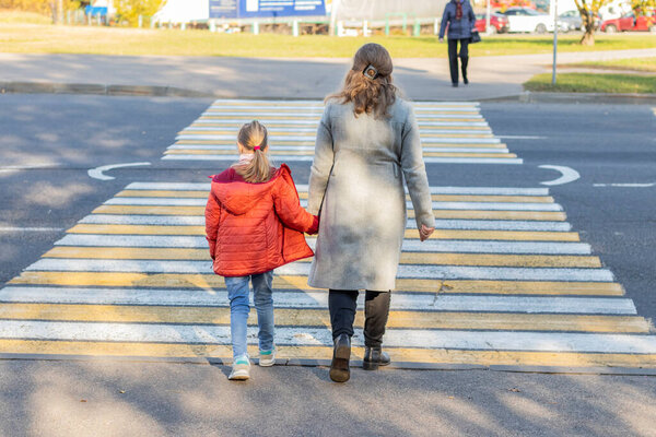 natural light. road. a mother and a child with white hair cross a pedestrian crossing.