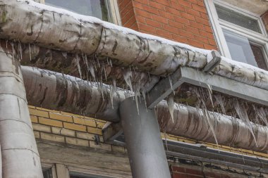 street lighting. a building through which a metal pipe wrapped with a thermal coating passes. there are damages and deformations, water flows and freezes and icicles have formed.