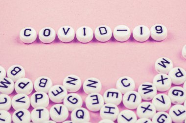 Covid 19 kelimeleri pembe ya da beyaz arka planda harflerle yazılmıştır. Yakınlarda bir sürü oyuncak yazıları var.
