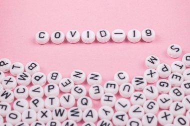Covid 19 kelimeleri pembe ya da beyaz arka planda harflerle yazılmıştır. Yakınlarda bir sürü oyuncak yazıları var.