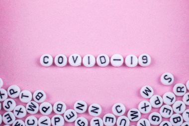 Covid 19 kelimeleri pembe ya da beyaz arka planda harflerle yazılmıştır. Yakınlarda bir sürü oyuncak yazıları var.