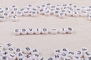 Covid 19 kelimeleri pembe ya da beyaz arka planda harflerle yazılmıştır. Yakınlarda bir sürü oyuncak yazıları var.