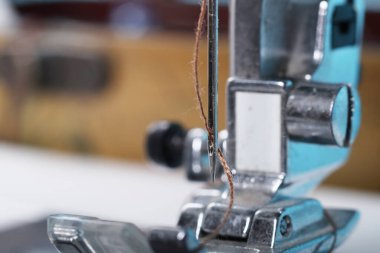 Dikiş makinesi. İlgi odağı olan bir ayak ve bir iğne. Yakın plan. Çerçevede hafif bir boyama var..