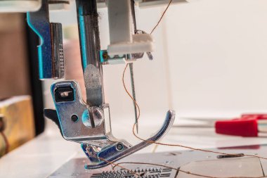 Dikiş makinesi. İlgi odağı olan bir ayak ve bir iğne. Yakın plan. Çerçevede hafif bir boyama var..