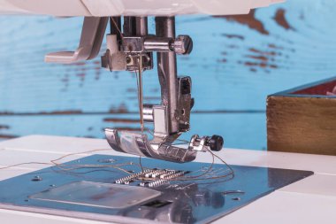 Dikiş makinesi. İlgi odağı olan bir ayak ve bir iğne. Yakın plan. Çerçevede hafif bir boyama var..