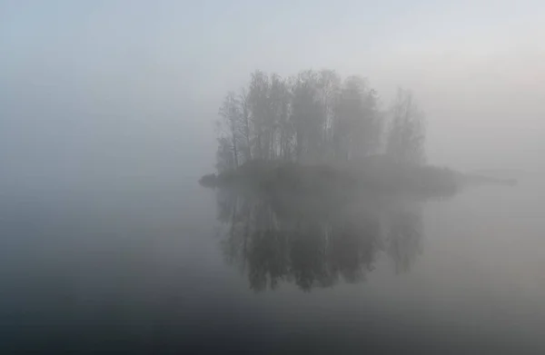 Ранним утром с видом на туманное озеро и маленький остров — стоковое фото