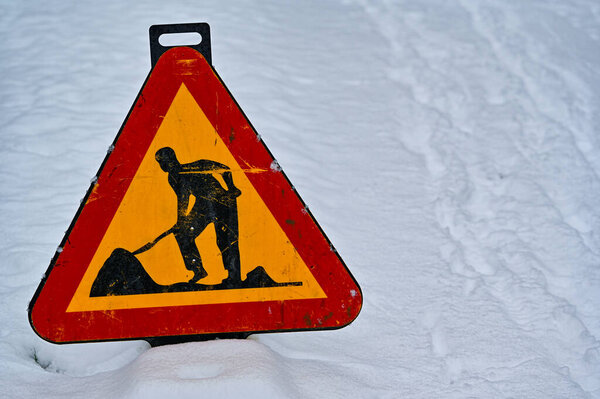 warning sign for road work standing in snow