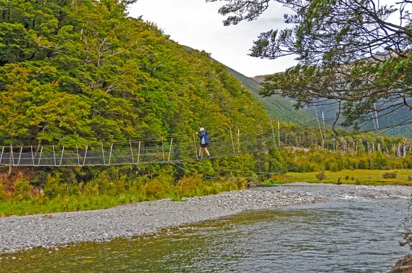 Escursionista Attraversare un ponte sospeso su un fiume selvaggio — Foto Stock