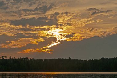 Günbatımında Ontario 'daki Quetico İl Parkı' ndaki Saganaga Gölü 'nde bulutlardan kaçmaya çalışan güneş ışığı.