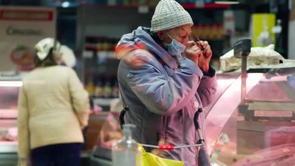 Старушка покупает мясо в магазине. Пенсионер стоит у витрины — стоковое видео