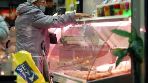 Egy idős hölgy húst vásárol egy boltban. Egy nyugdíjas áll egy üvegvitrinben. — Stock videók