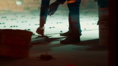 Tulumlu adamlar fayansları güvene almak için yere çimento dökerler. İnşaat işçileri