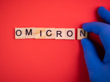 Delta 'nın yerine Omicron versiyonu. Koronavirüsün yeni tehlikeli bir türü olan COVID-19 Omicron ortaya çıktı. Mavi eldivenler hazır. Renkli kırmızı arkaplanda omikron sözcükleri
