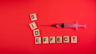 Şırınga solüsyonla dolu. Renkli kırmızı kağıt dokusu üzerinde sözcüklerin yan etkisi. Kavram. Aşı aşısının yan etkisi ya da zehirlenme endişesi. Uzayı kopyala Tasarımı düzenle.