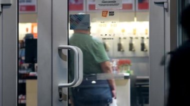 Ziyaretçi, gece yarısı bira dükkanında tezgahın önünde duruyor. Dükkanın cam kapıları.